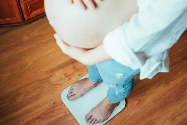 Image of woman weighing herself and experiencing weight gain through pregnancy Poole